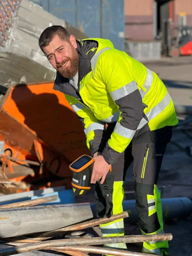 Medarbetare i varselkläder kontrollerar metallrör med en handhållen metallanalysator
